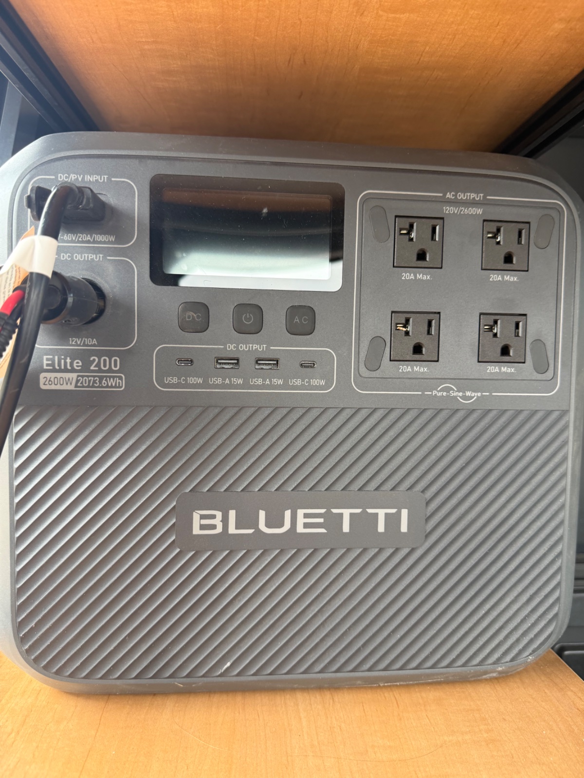 Bluetti Elite 200 portable power station displaying 2400W capacity and 2073.6Wh battery with AC outlets, USB ports, and DC inputs on wooden surface