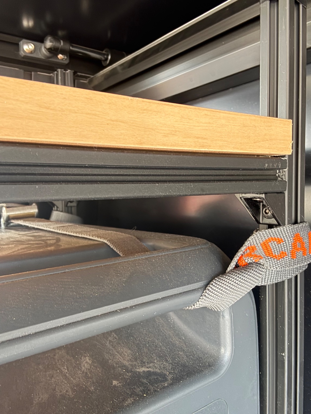 Truck bed storage system with wooden shelf and gray drawer organizer secured with orange and gray straps