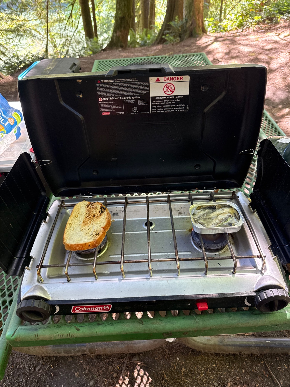 Coleman camping stove with toasted bread and butter dish cooking outdoors in a forest setting