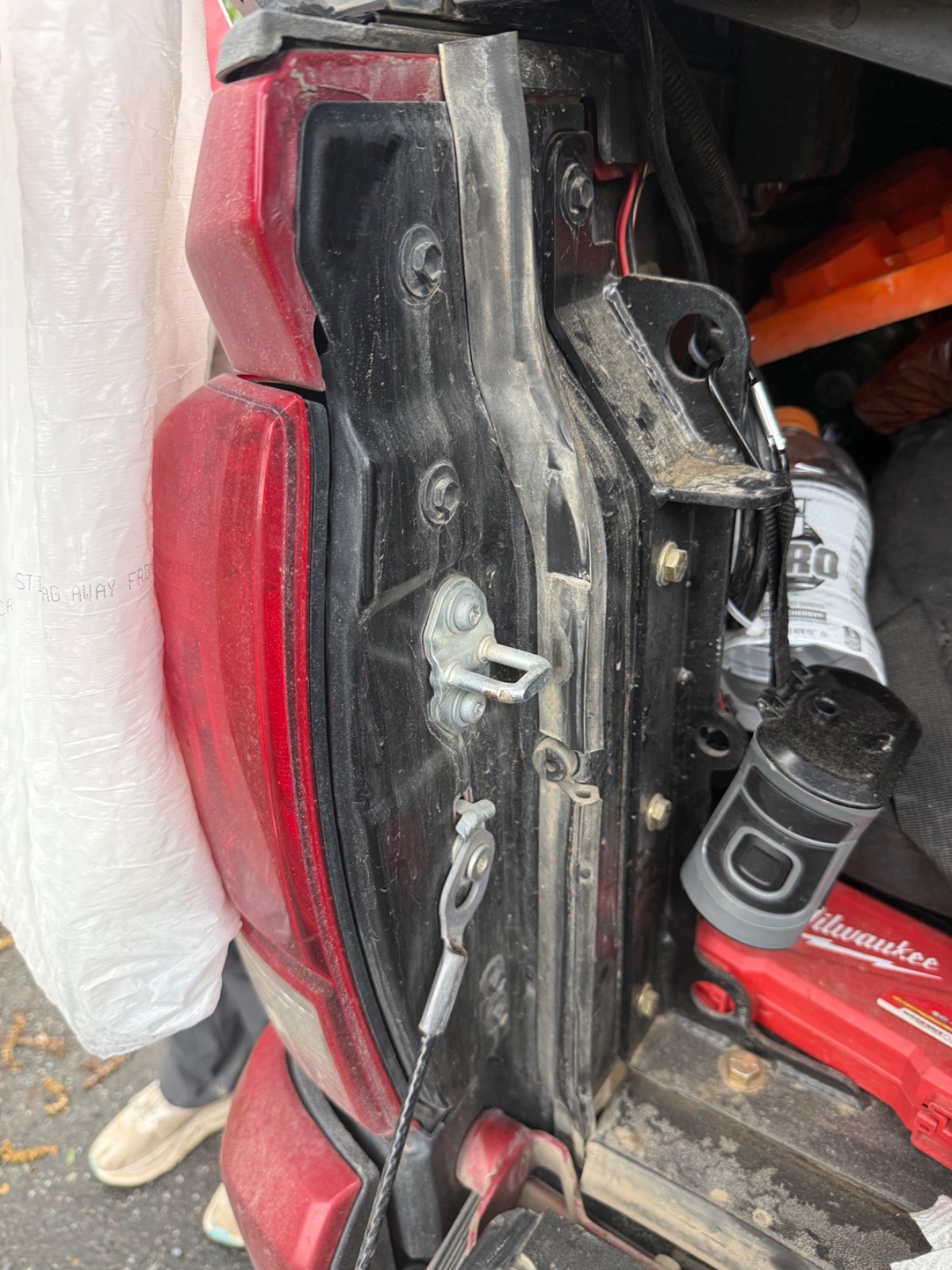 Close-up of vehicle door hinge mechanisms and red tail light assembly with Milwaukee tool visible in background