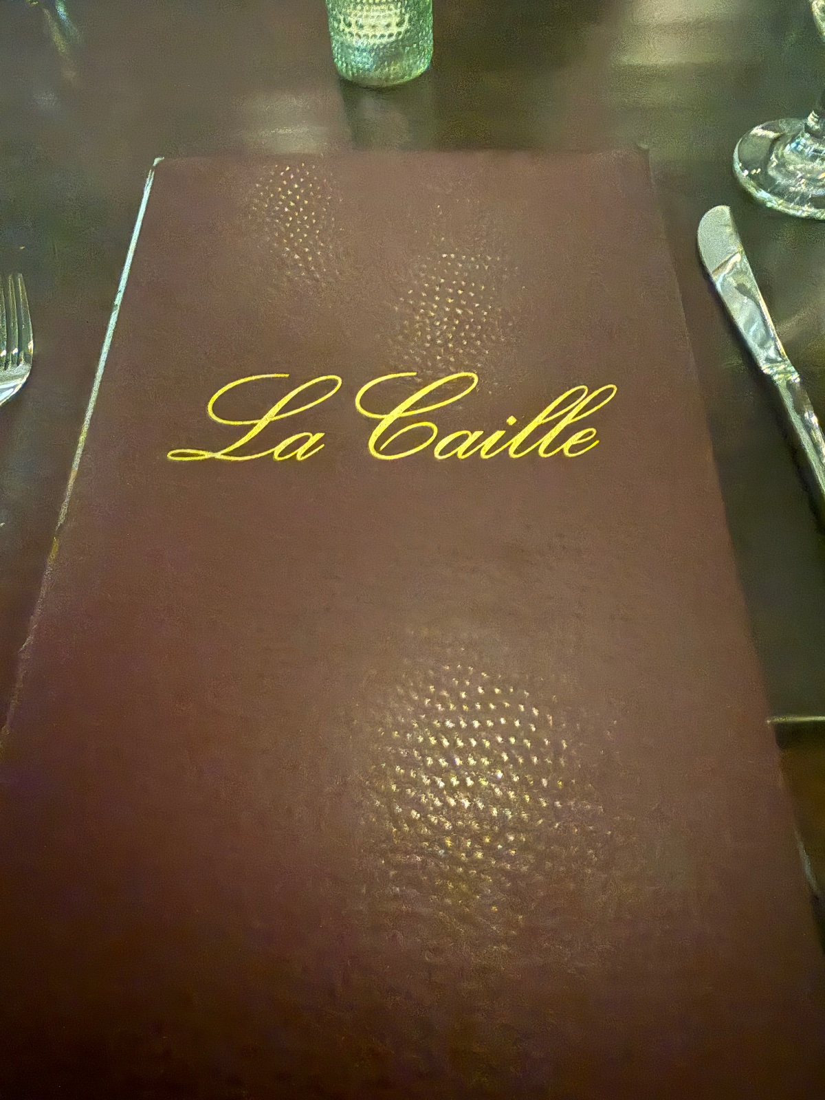 Fine dining menu cover for La Coille restaurant with elegant gold script lettering on burgundy leather at an upscale table setting