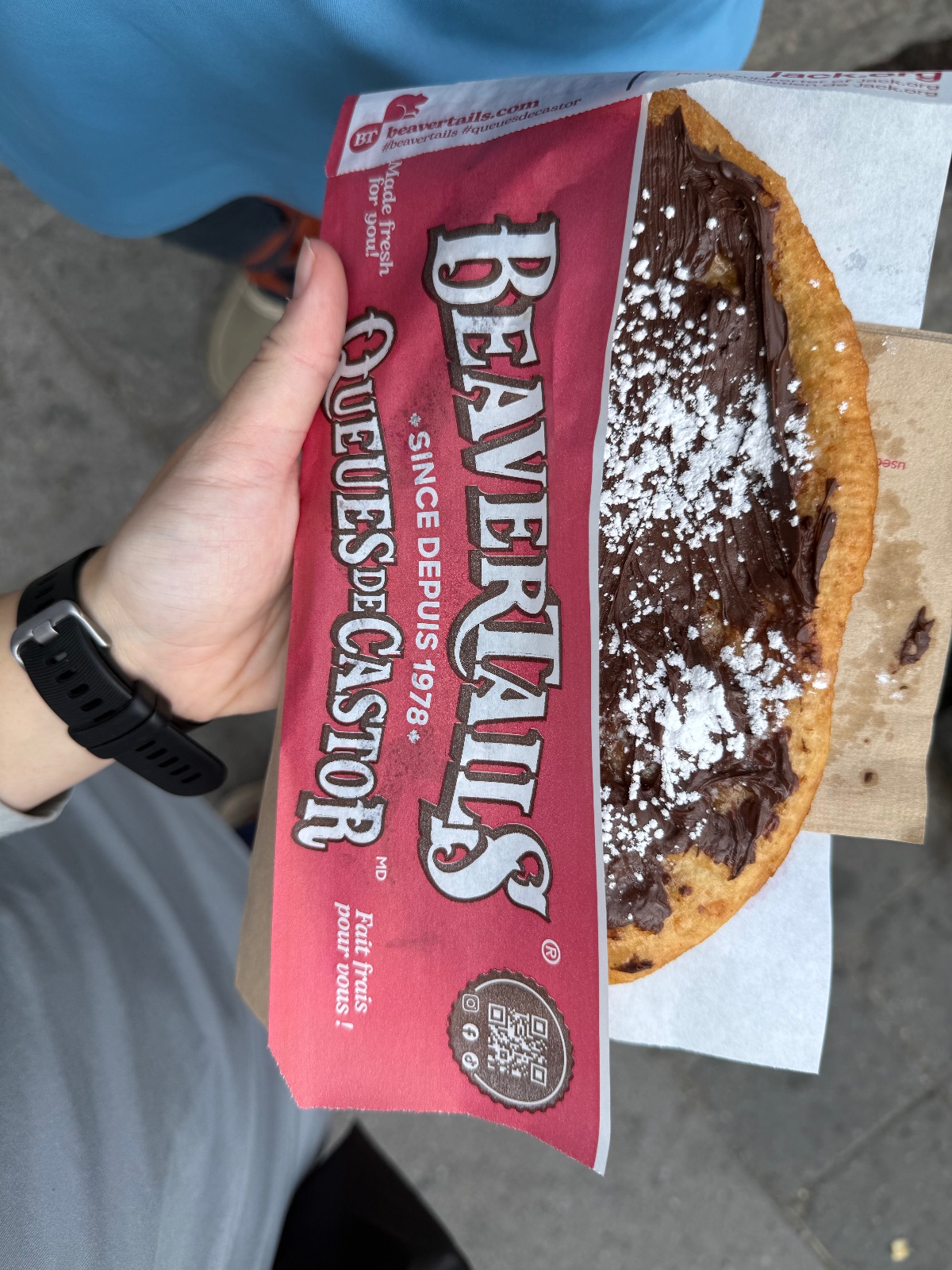 Hand holding a red Bavarian Bites pastry box with a chocolate-filled pastry dusted with powdered sugar outdoors