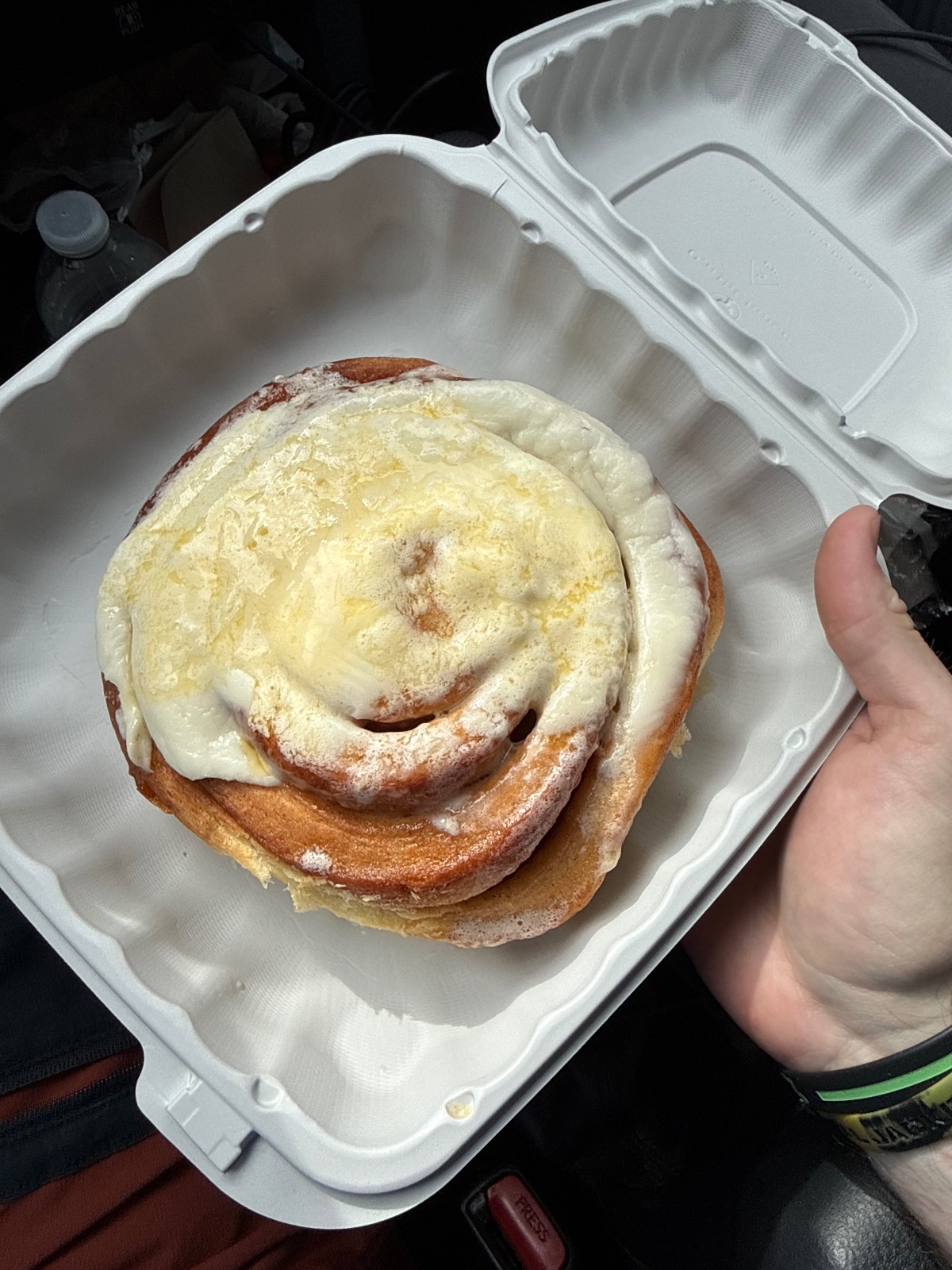 Cinnamon roll with cream cheese frosting held in a white foam container during an outdoor adventure