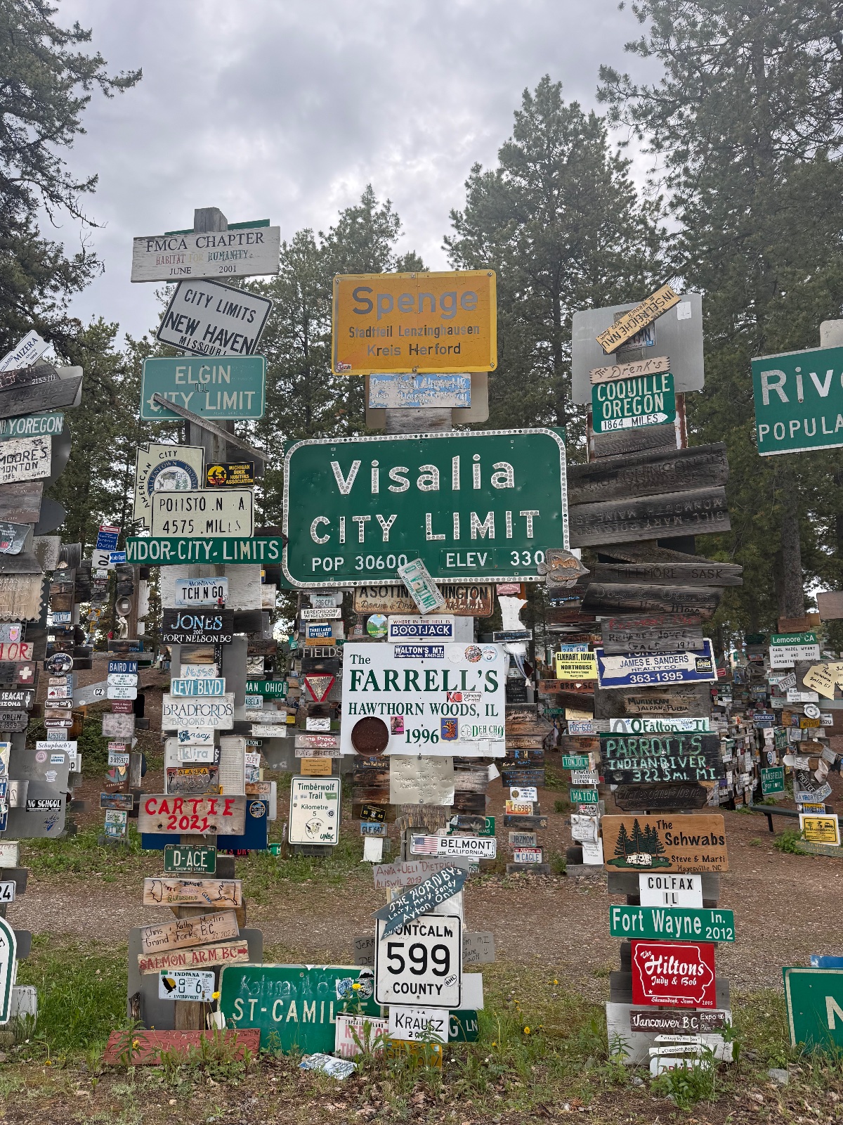 Visalia city limit sign surrounded by hundreds of road signs and memorabilia nailed to wooden posts under overcast skies in Oregon