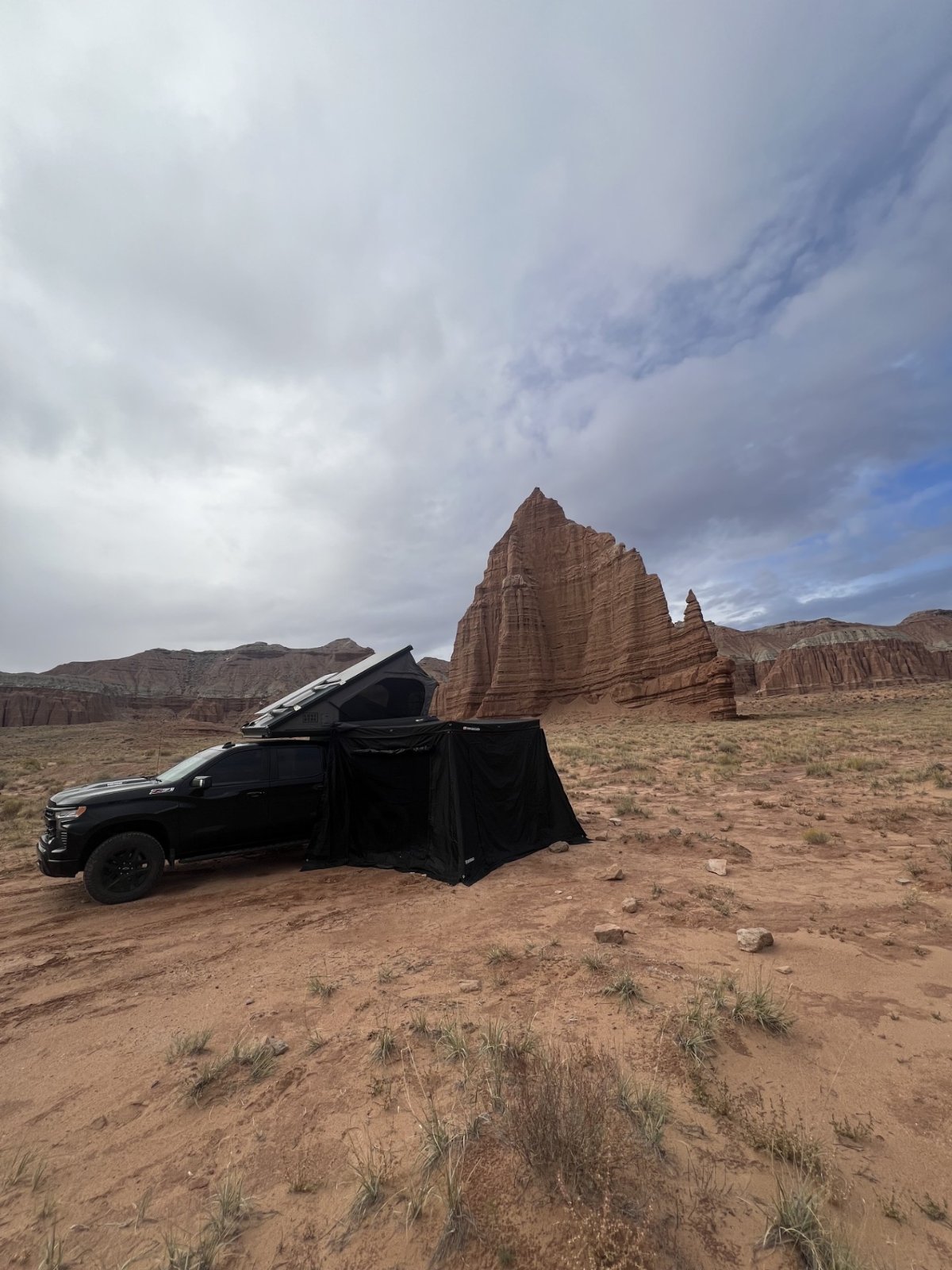 Black pickup truck with roof tent and awning deployed in desert landscape with red rock formations and stormy sky