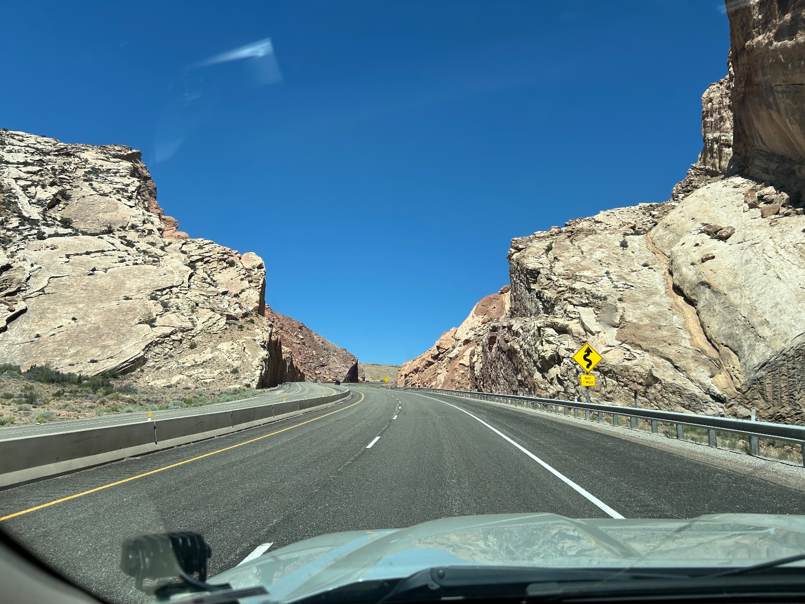 View from vehicle dashboard driving through a rocky canyon pass with 6 mph curve warning sign on a clear desert highway