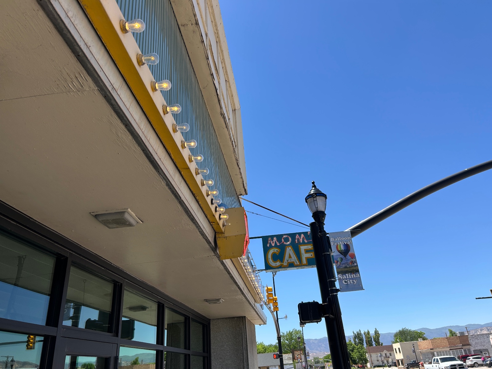 Mom's Cafe storefront with yellow awning and string lights on a sunny day in Salina City, mountains visible in background