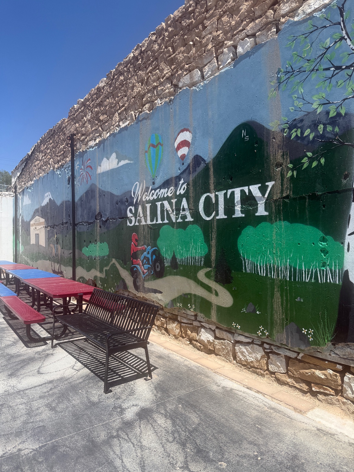 Welcome to Salina City mural painted on a stone building with picnic tables and benches in foreground under clear blue sky