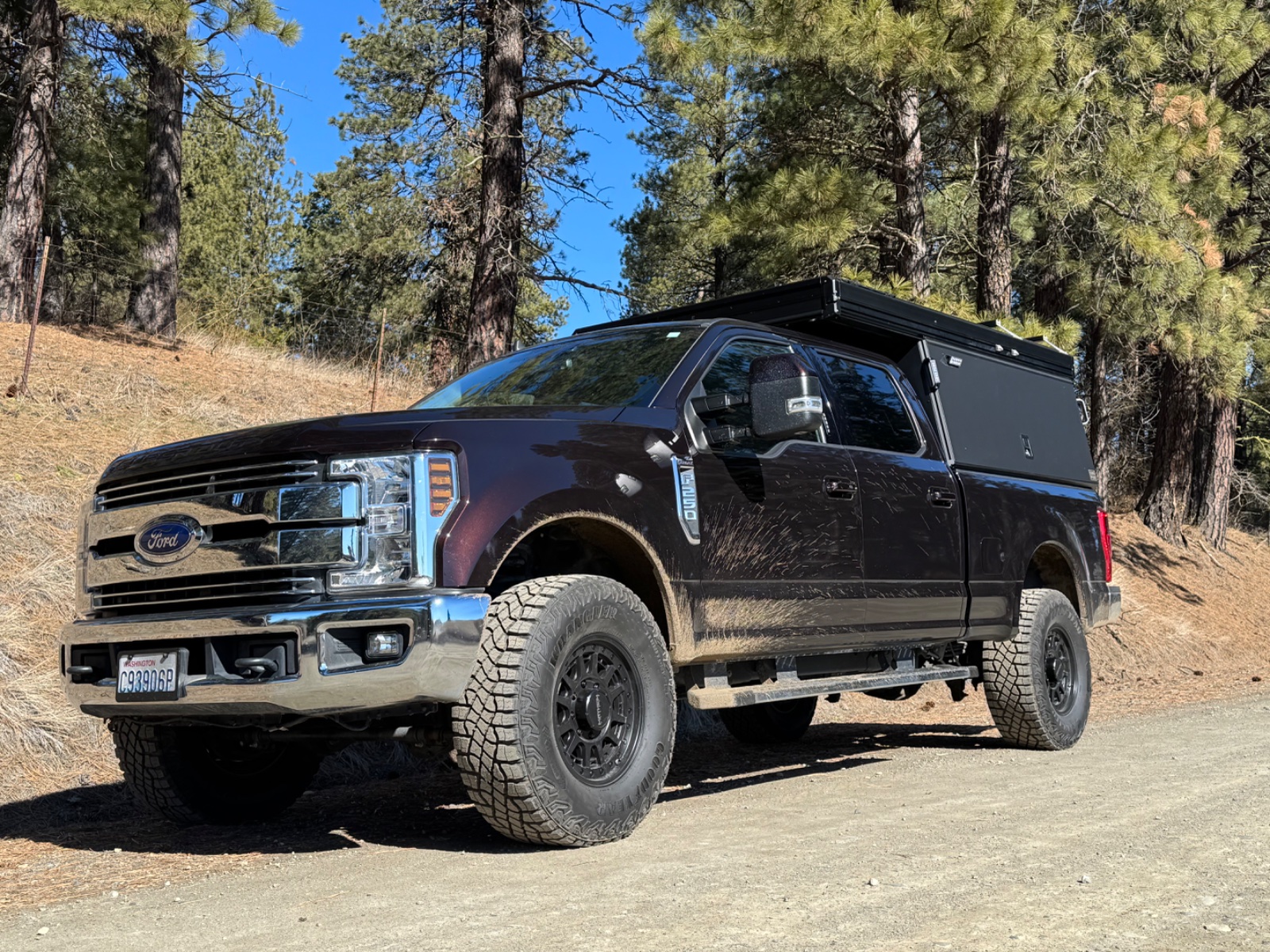 Modified Ford F-250 Super Duty with lifted suspension and roof rack parked on dirt road surrounded by pine forest