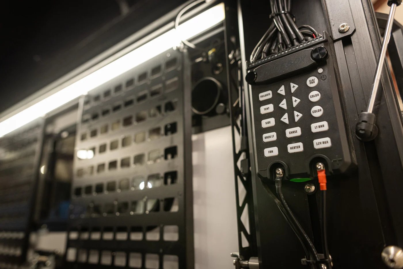 Close-up of a vehicle control panel with illuminated buttons for lights, heating, and auxiliary systems in an off-road setup