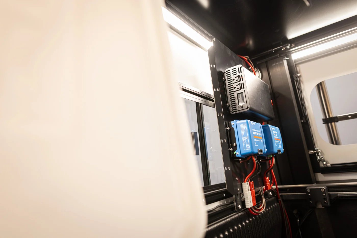 Close-up of 3D printer electronics mounted on black frame showing blue power modules, heatsink, and red wiring with white wall backdrop