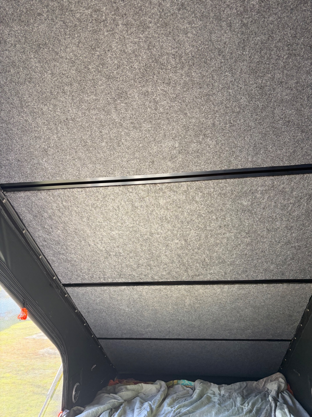 Interior view of a vehicle's roof with gray headliner panels and black trim, showing bedding stored below