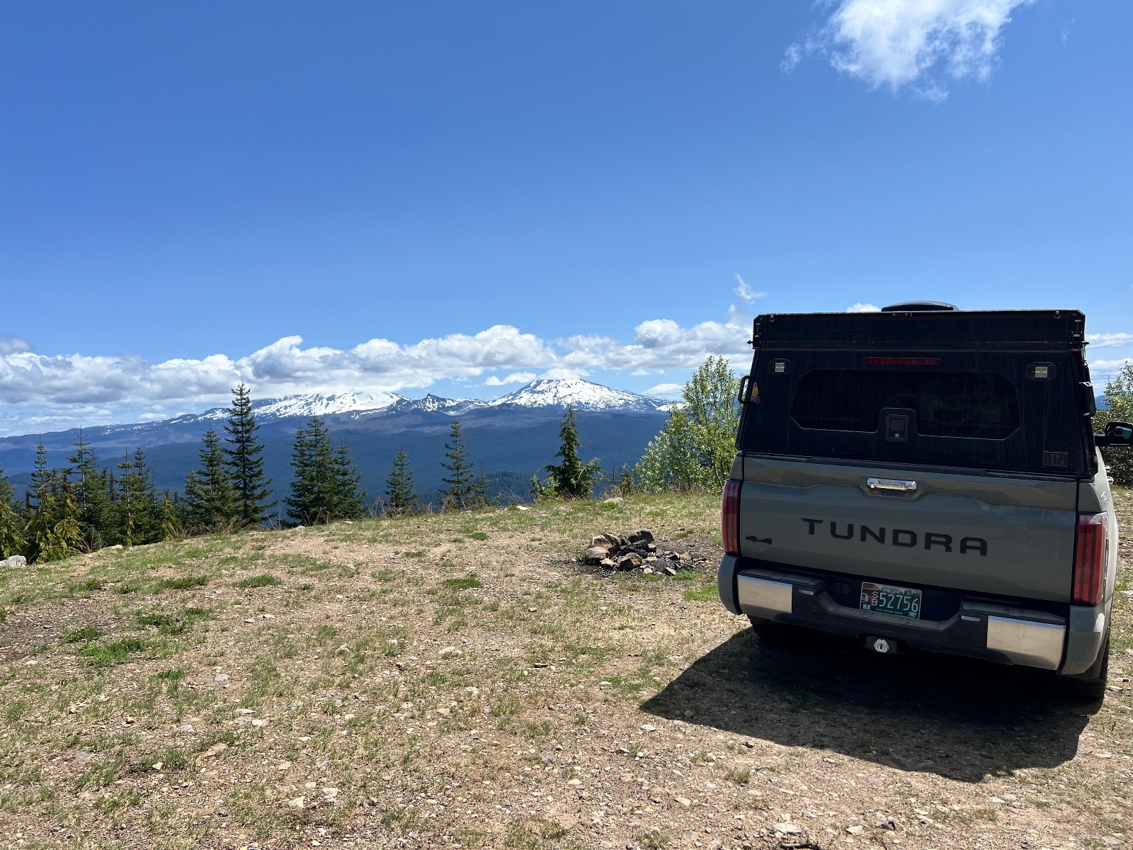 Toyota Tundra parked at a mountain overlook with snow-capped peak, coniferous forest, and clear blue sky with white clouds