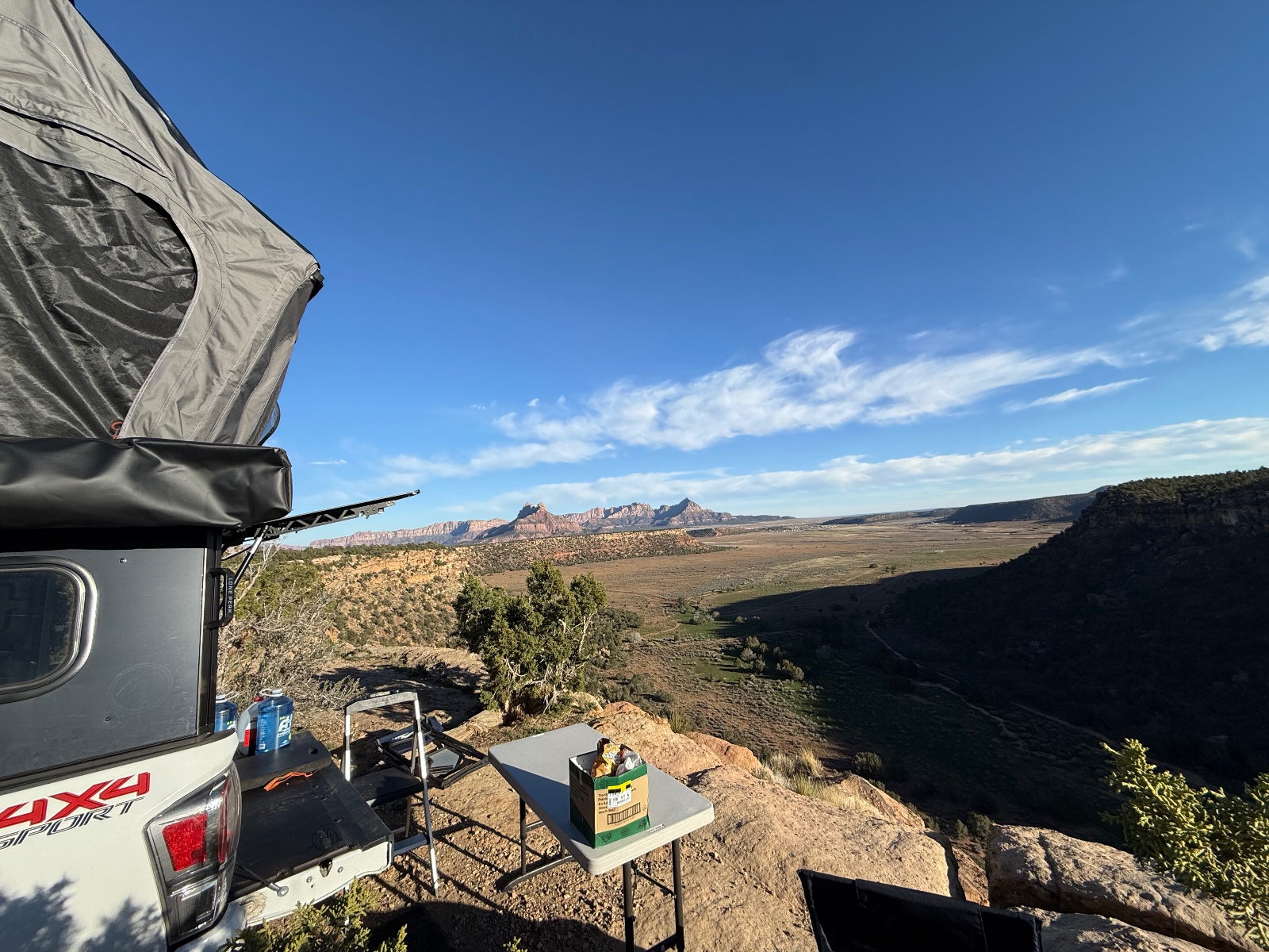 White pickup truck with rooftop tent and awning set up at a high desert overlook with red rock formations and valley views in the background