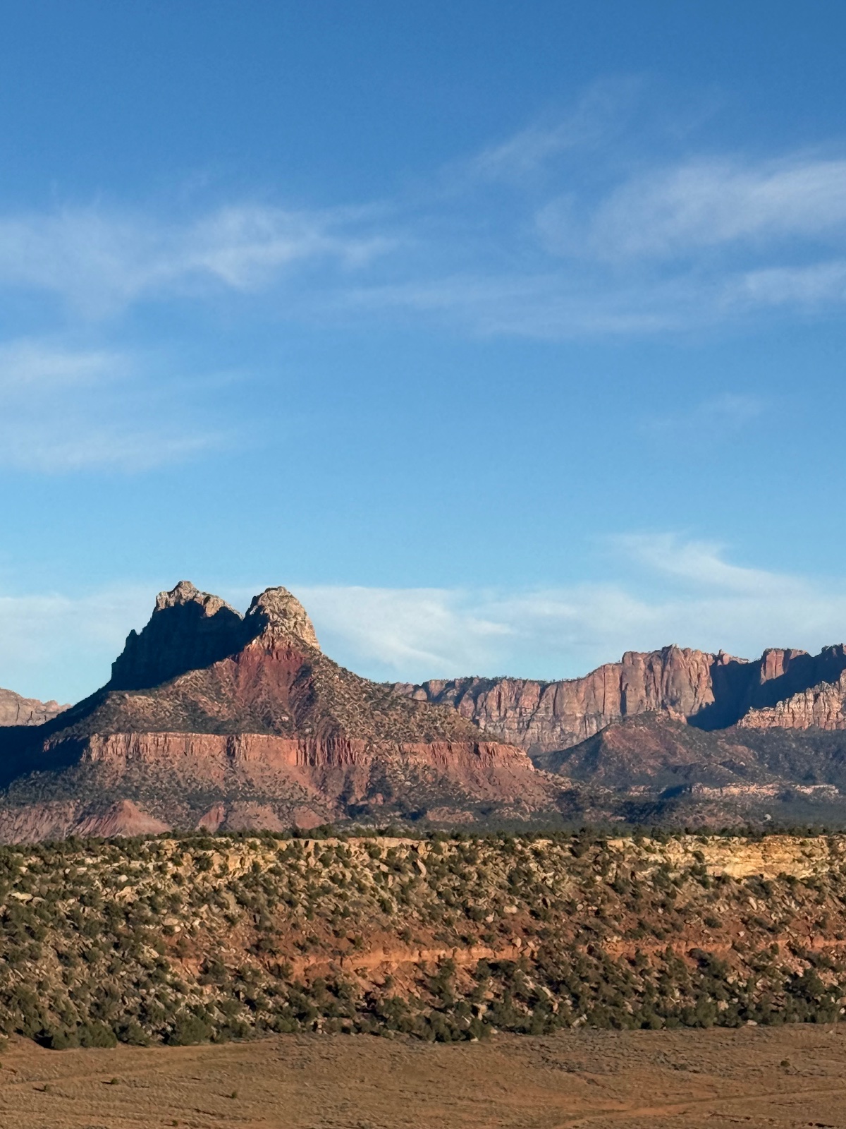 Distinctive red rock formations and desert mountains under clear blue sky with sparse desert vegetation in foreground