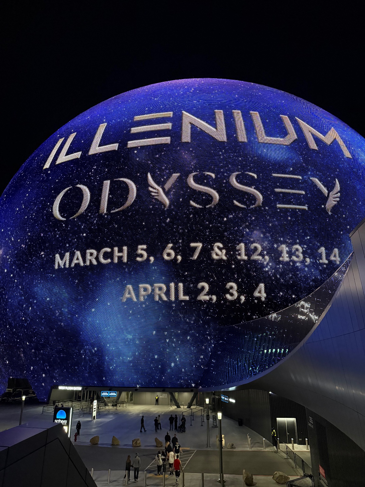 Illuminated blue spherical planetarium building displaying 'Illinium Odyssey' with event dates in March and April at night