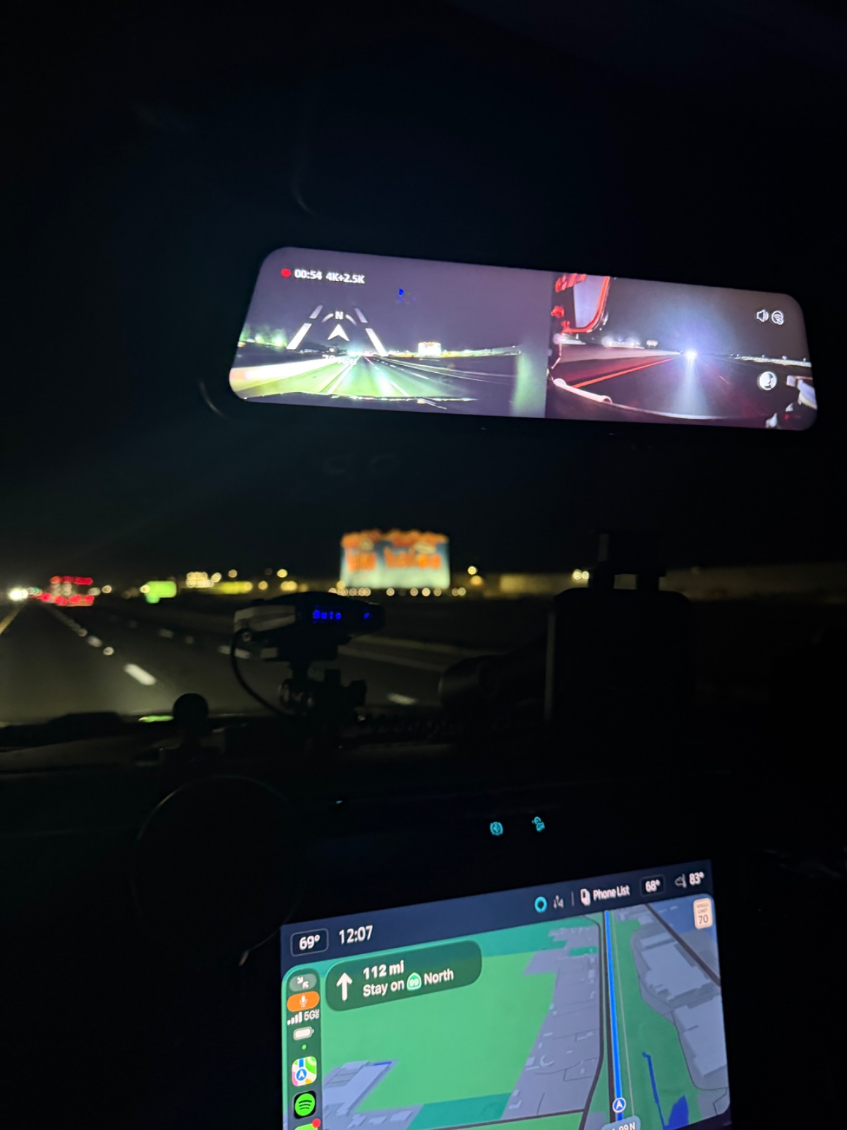 Nighttime highway driving view showing dual dashcam feeds on upper display and navigation map on lower screen while traveling north on interstate