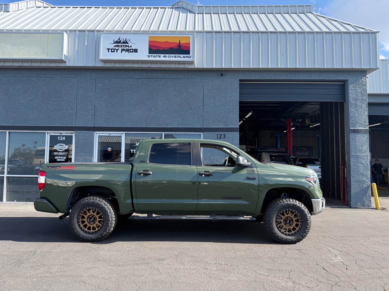 Lifted Toyota Tundra in sage green with bronze wheels parked outside Arizona Toy Pros shop in desert setting