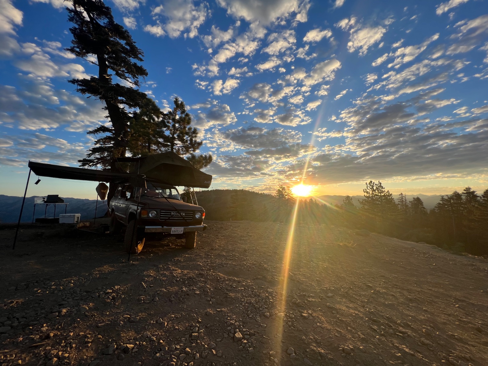 Toyota pickup truck with roof rack and awning parked on mountain overlook at sunset with pine trees and valley views