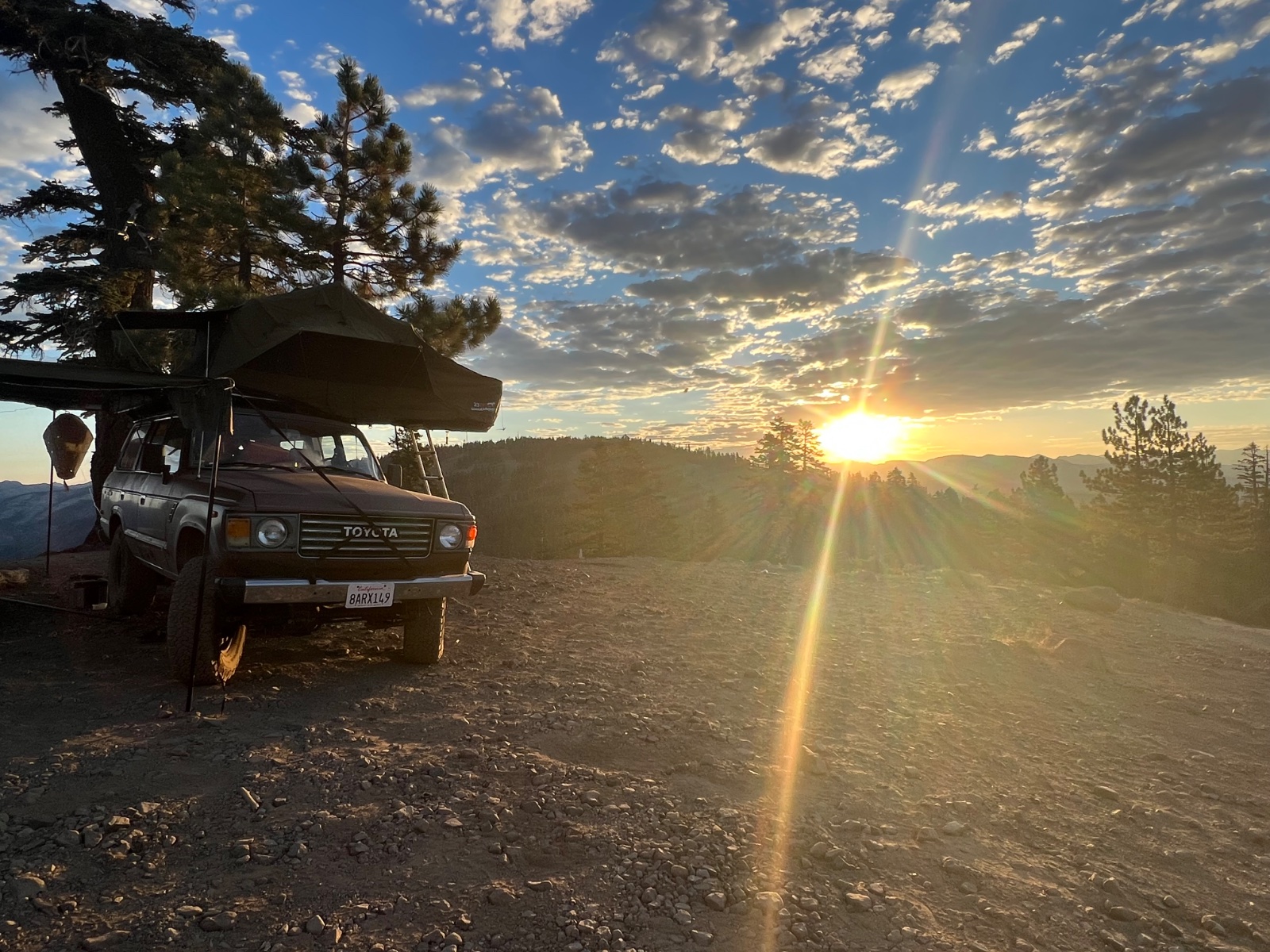 Toyota pickup truck with roof tent parked on mountain overlook at sunset with pine trees and forested valleys in background
