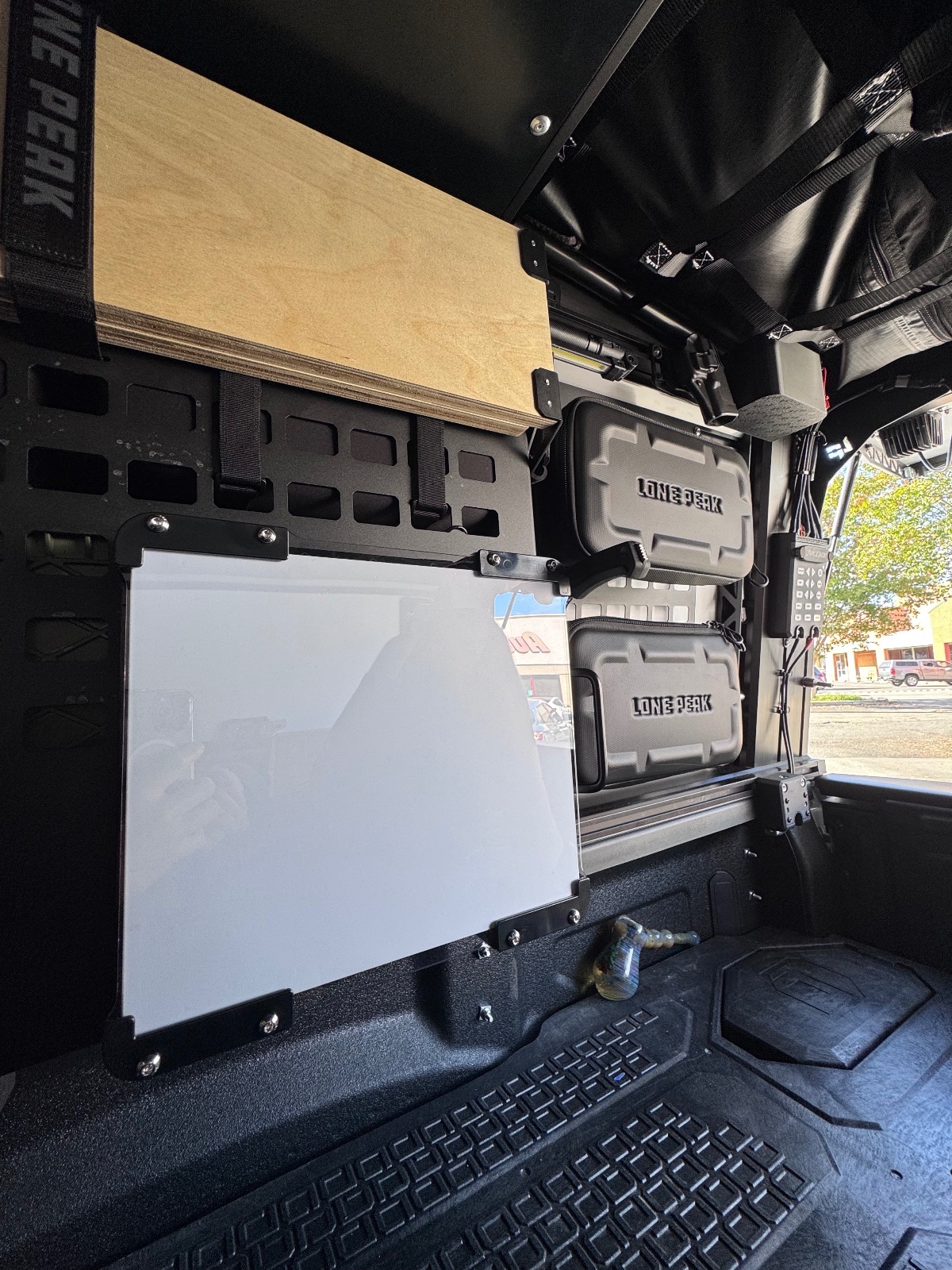 Interior view of an overland vehicle showing white storage boxes labeled Lone Peak, wooden roof rack, and organized gear setup with desert landscape visible outside