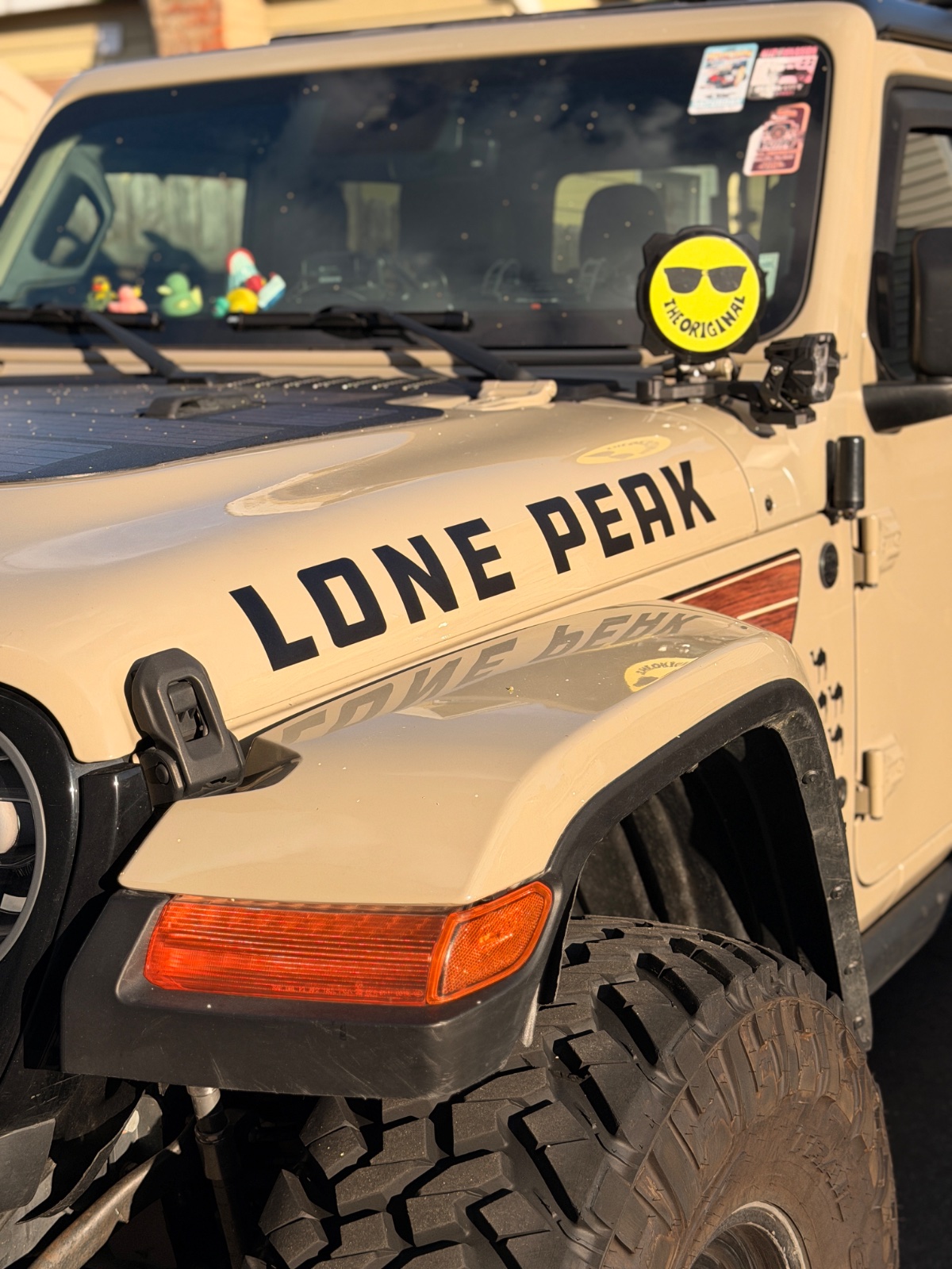 Tan Jeep Wrangler named 'Lone Peak' with aftermarket bumper, winch, and all-terrain tires, decorated with dashboard figurines and stickers