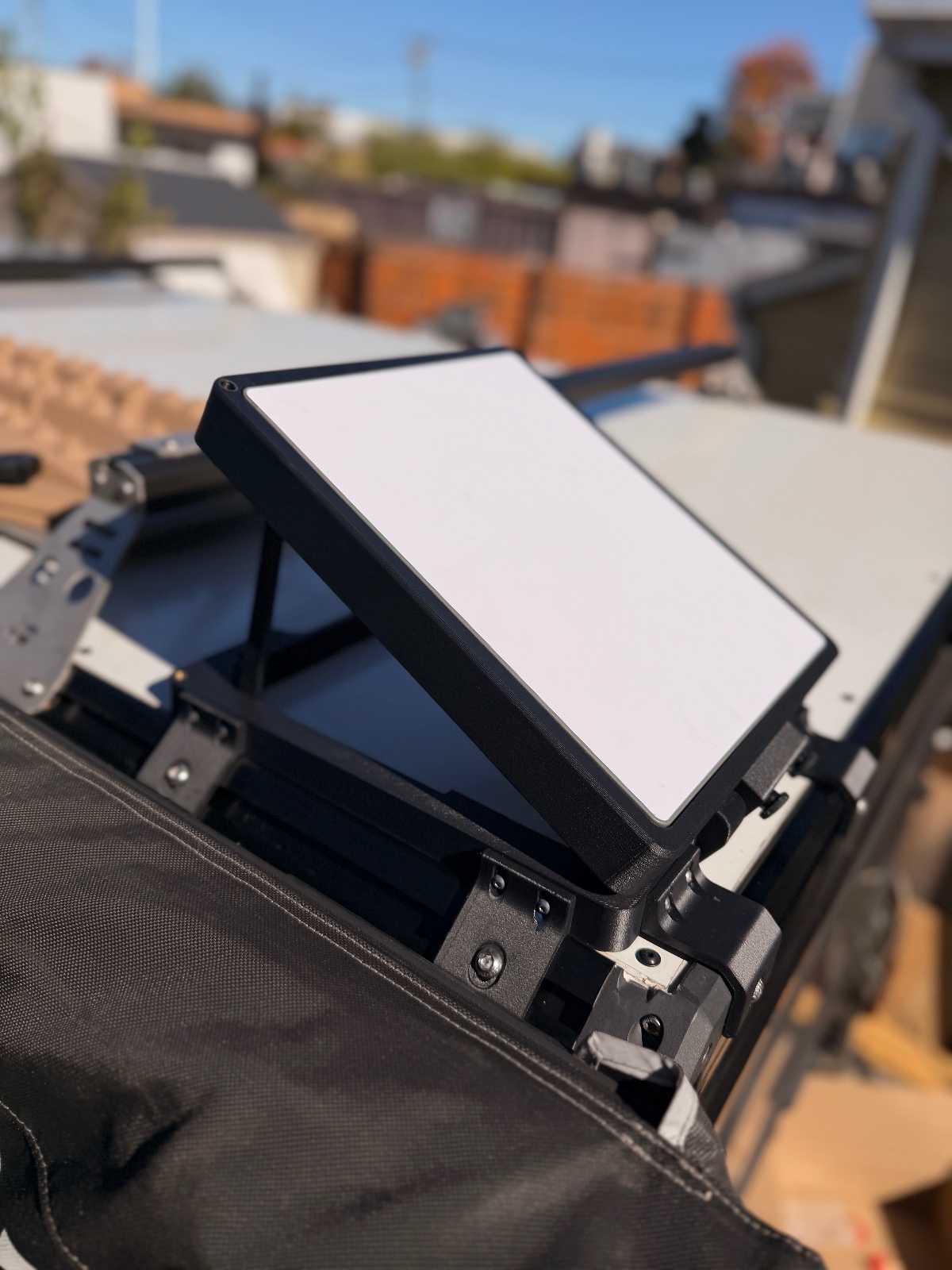 Professional video production monitor mounted on camera rig at outdoor rooftop location with construction site and buildings visible in background