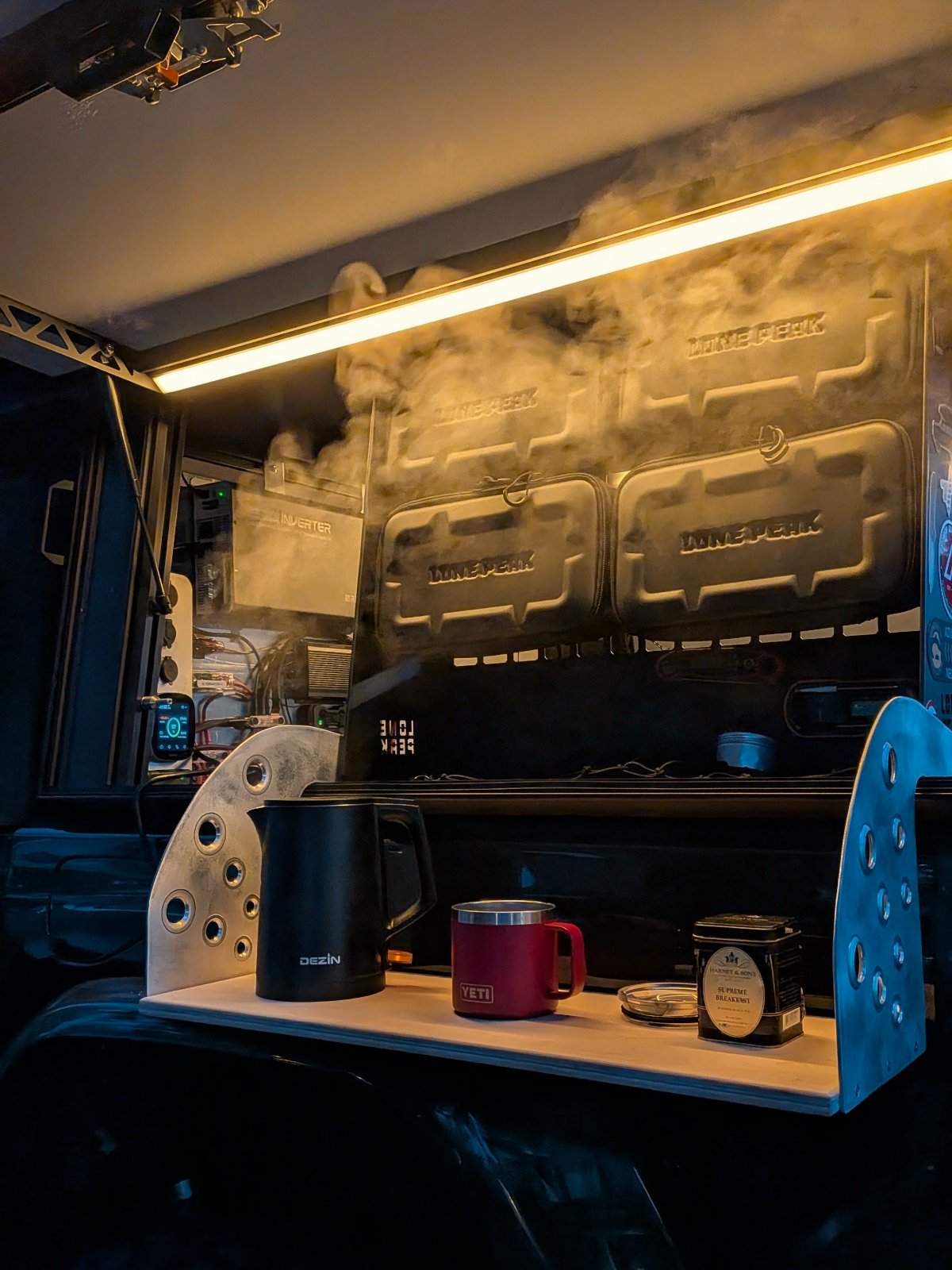 Custom overlanding trailer interior with golden lighting, displaying YETI drinkware, Ozin gear, and decorative metal accents alongside various camping equipment