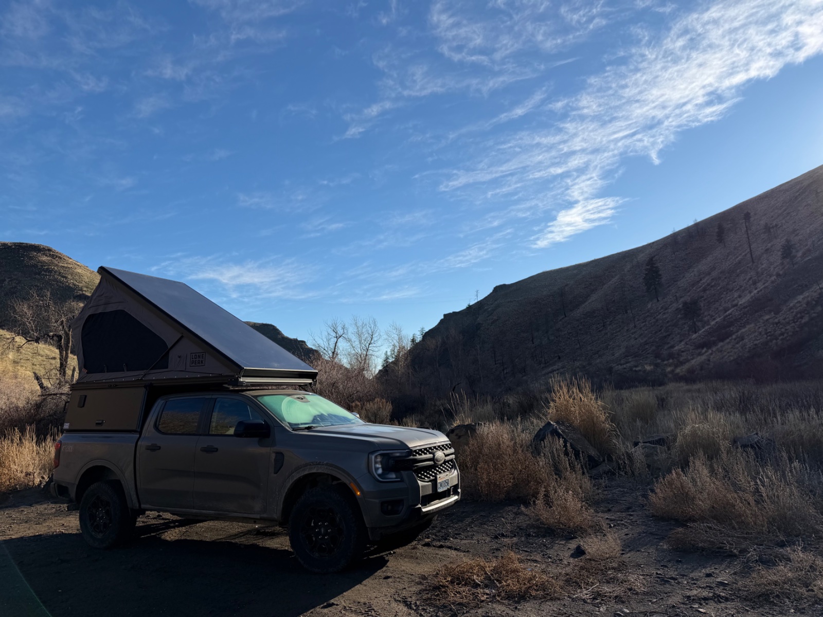 Silver Ford Ranger with roof-mounted tent in a scenic desert canyon valley under blue sky with sparse vegetation